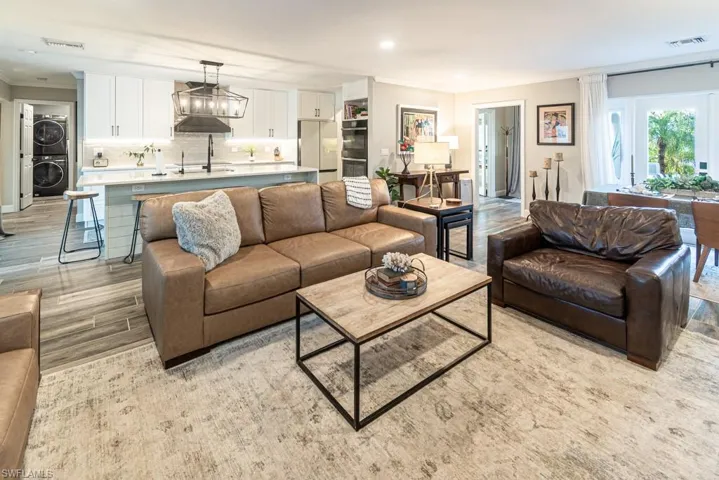 Living room featuring light wood-style flooring, crown molding, stacked washing maching and dryer, and visible vents