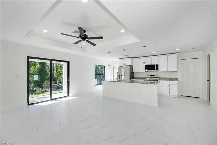 Kitchen with white cabinetry, dark stone countertops, a tray ceiling, a kitchen island with sink, and appliances with stainless steel finishes