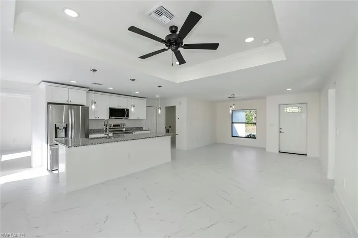 Kitchen with dark stone counters, white cabinets, a raised ceiling, an island with sink, and appliances with stainless steel finishes