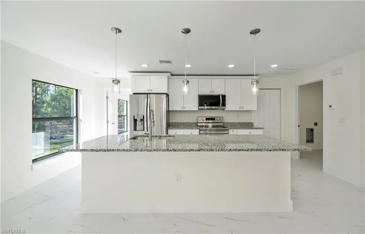 Kitchen with a wealth of natural light, white cabinetry, stainless steel appliances, and hanging light fixtures