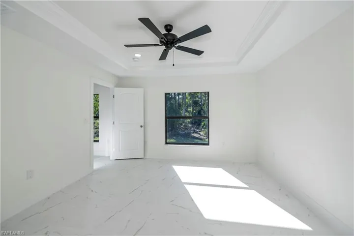 Empty room featuring ceiling fan, a raised ceiling, and crown molding