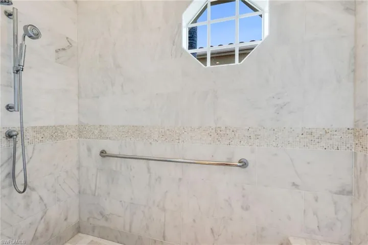 The large shower has marble walls to the ceiling, with complementing mosaic inlays.