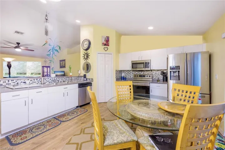 Kitchen with stainless steel appliances, vaulted ceiling, decorative backsplash, and white cabinetry