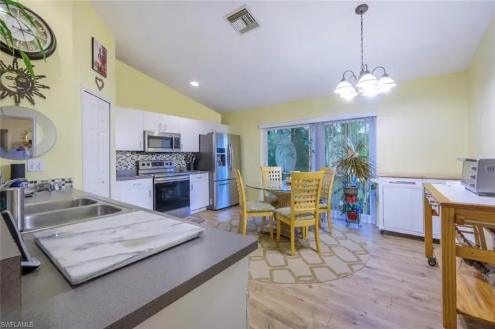 Kitchen with a notable chandelier, tasteful backsplash, white cabinetry, appliances with stainless steel finishes, and sink