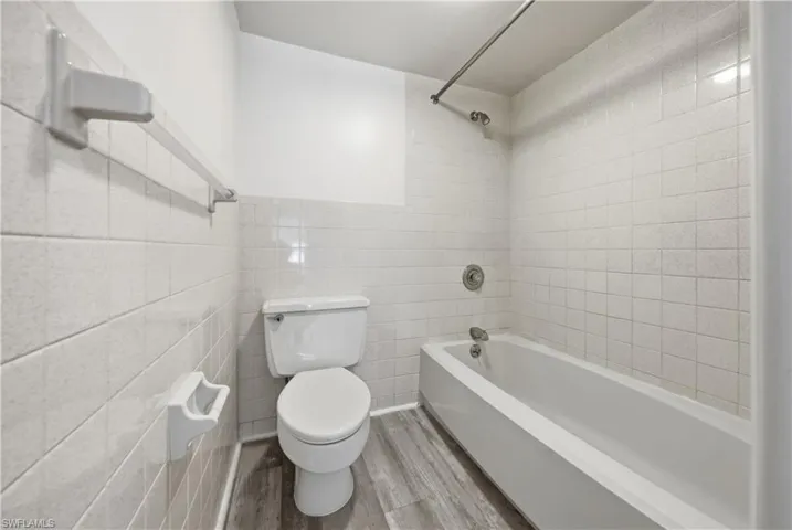 Full bathroom with tile walls, bathing tub / shower combination, and light wood-style floors