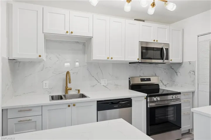 Kitchen with stainless steel appliances, white cabinets, light stone counters, and backsplash