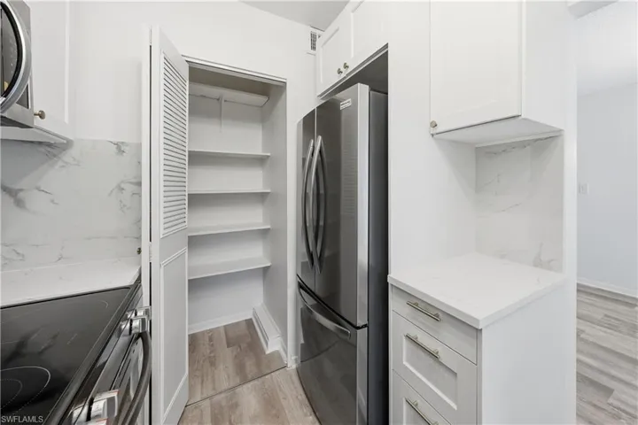 Kitchen featuring stainless steel appliances, light stone counters, white cabinets, and light wood-style floors