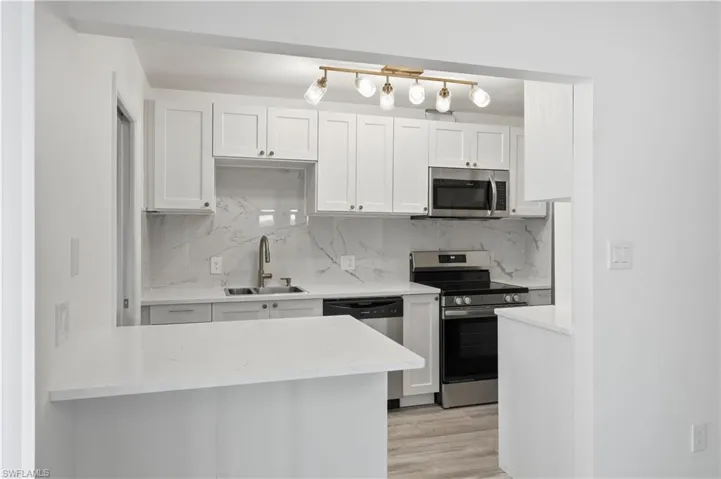 Kitchen with stainless steel appliances, white cabinetry, light wood-type flooring, and backsplash