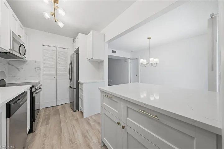 Kitchen with light stone counters, stainless steel appliances, light wood-style floors, and white cabinetry