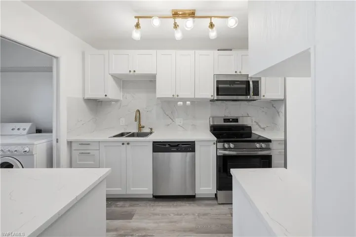 Kitchen featuring stainless steel appliances, white cabinets, washer / clothes dryer, light wood-style floors, and light stone counters