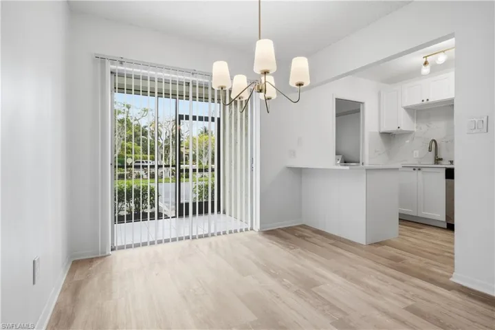 Kitchen featuring white cabinets, light wood-type flooring, suspended lighting, and decorative backsplash