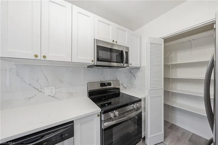 Kitchen featuring stainless steel appliances, white cabinetry, backsplash, and light stone countertops