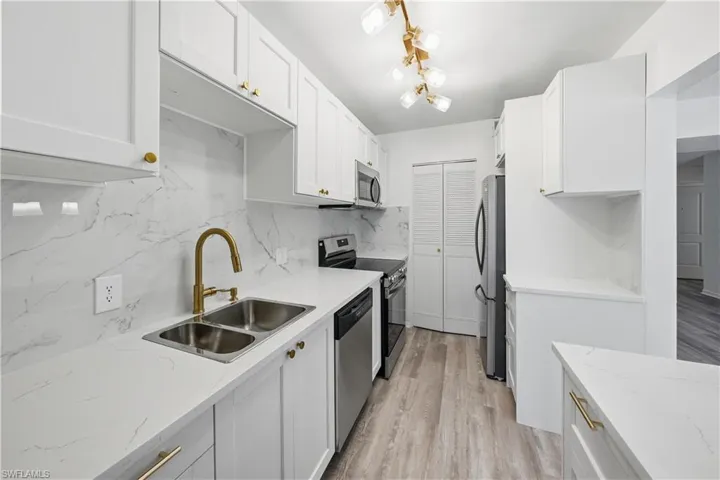 Kitchen with stainless steel appliances, white cabinetry, backsplash, light stone countertops, and light wood-type flooring