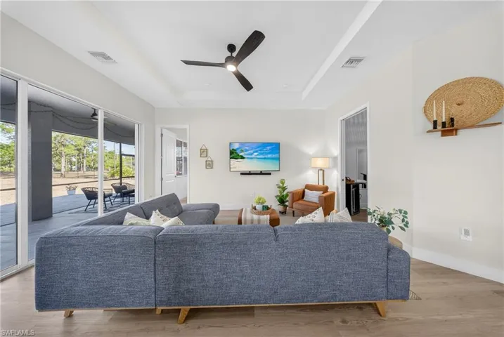 Living area with a ceiling fan, light wood-type flooring, a tray ceiling, and a sunroom