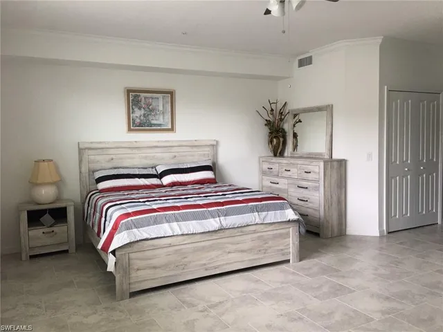 Bedroom with light tile patterned flooring, a closet, ornamental molding, and ceiling fan