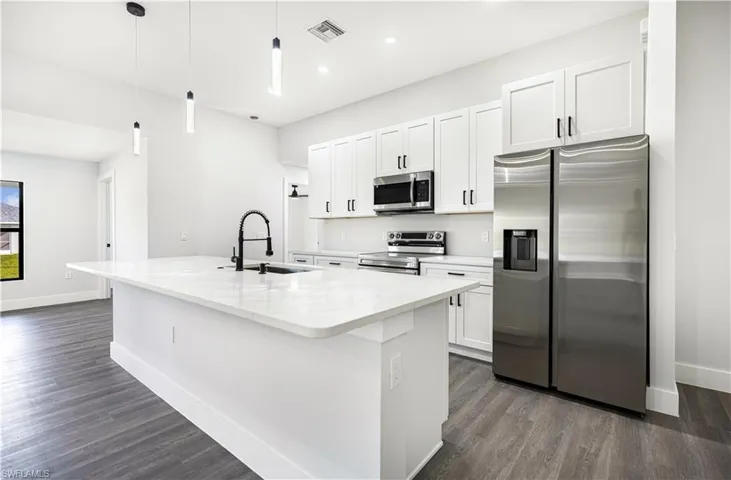 Kitchen featuring white cabinetry, hanging light fixtures, appliances with stainless steel finishes, and a kitchen island with sink