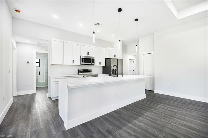 Kitchen featuring an island with sink, stainless steel appliances, pendant lighting, white cabinets, and dark hardwood / wood-style floors