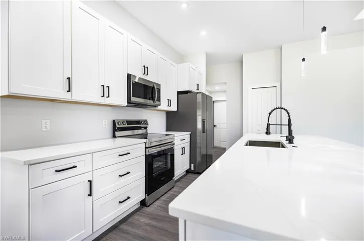 Kitchen with dark wood-type flooring, appliances with stainless steel finishes, and white cabinets