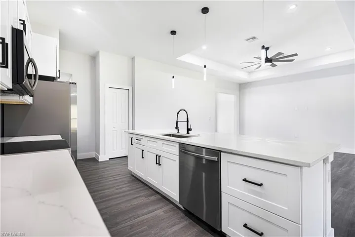 Kitchen with light stone countertops, sink, hanging light fixtures, white cabinetry, and stainless steel appliances