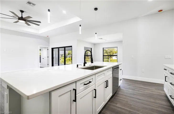 Kitchen featuring an island with sink, dark hardwood / wood-style flooring, hanging light fixtures, stainless steel dishwasher, and white cabinets