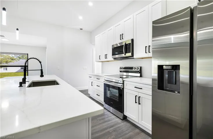 Kitchen with white cabinetry, light stone countertops, dark wood-type flooring, sink, and stainless steel appliances
