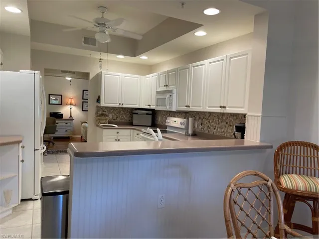 Kitchen featuring white cabinetry, white refrigerator, range, light tile patterned floors, and backsplash