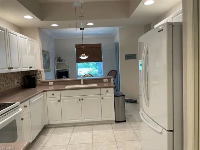 Kitchen with light tile patterned flooring, white cabinets, white appliances, sink, and backsplash