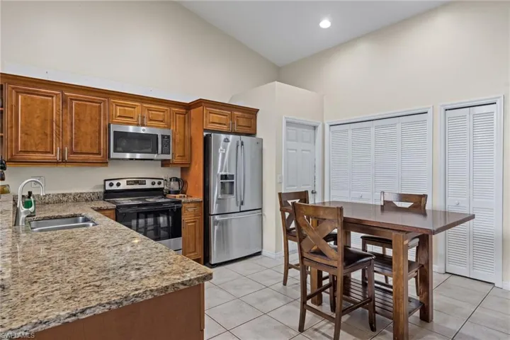 Kitchen featuring light stone counters, appliances with stainless steel finishes, brown cabinets, high vaulted ceiling, and light tile patterned flooring
