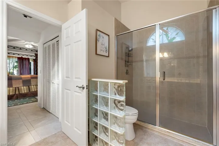 Bathroom featuring connected bathroom, a closet, a stall shower, light tile patterned floors, and a ceiling fan