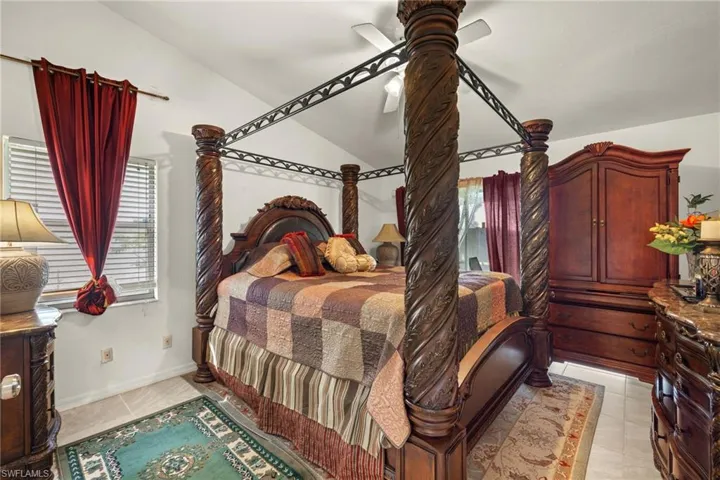 Bedroom featuring multiple windows, light tile patterned floors, vaulted ceiling, and a ceiling fan