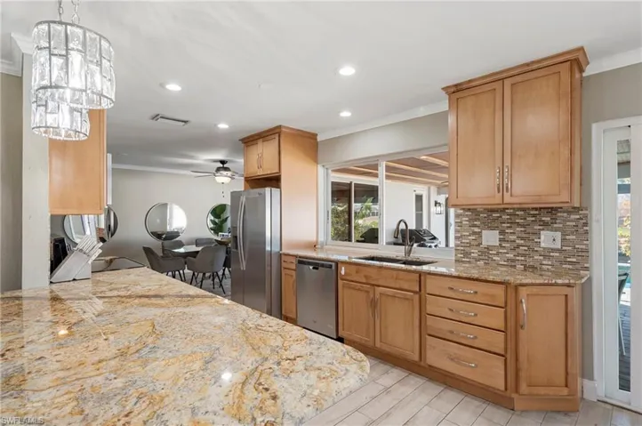 Kitchen featuring light stone counters, ornamental molding, appliances with stainless steel finishes, brown cabinetry, and recessed lighting