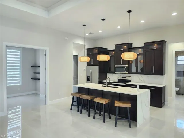 Kitchen with a center island with sink, decorative backsplash, stainless steel appliances, light tile patterned floors, and sink