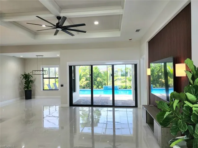 Living room with light tile patterned floors, coffered ceiling, ceiling fan, and plenty of natural light