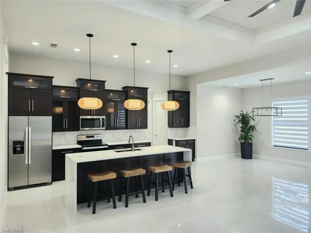 Kitchen featuring a kitchen island with sink, hanging light fixtures, light tile patterned floors, stainless steel appliances, and sink