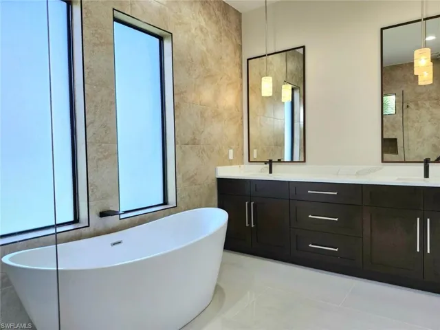 Bathroom with tile patterned floors, a bathing tub, tile walls, and dual bowl vanity