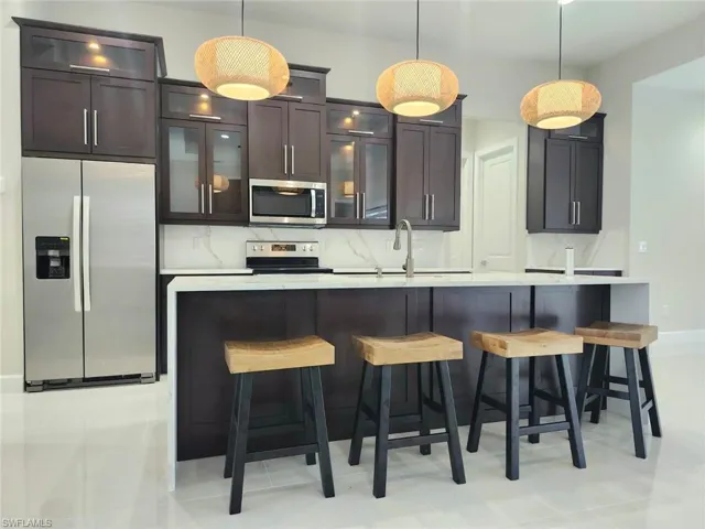 Kitchen with appliances with stainless steel finishes, dark brown cabinets, decorative light fixtures, and light tile patterned floors