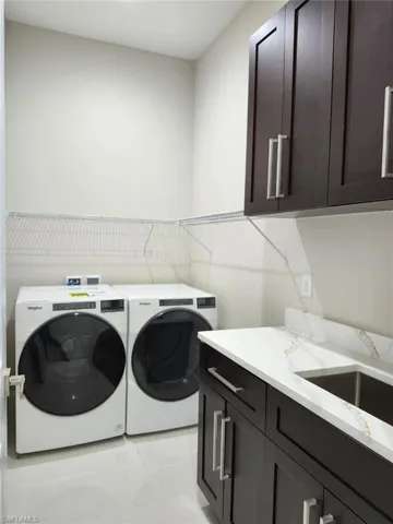 Clothes washing area featuring separate washer and dryer, cabinets, light tile patterned floors, and sink