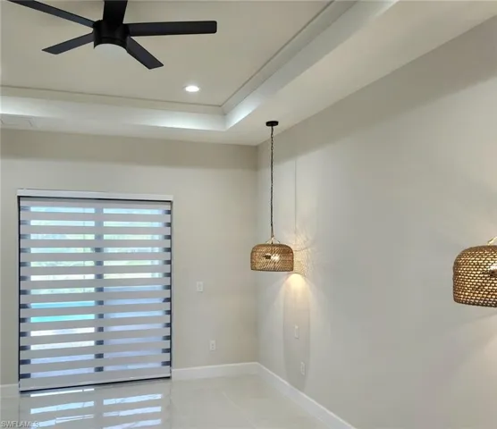 Empty room with ceiling fan, a raised ceiling, and light tile patterned floors
