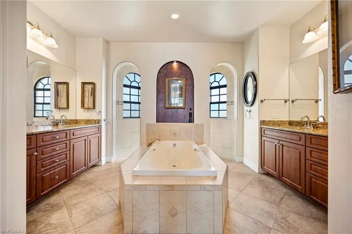 Bathroom with a tub with jets, walk in shower, plenty of natural light, two vanities, and recessed lighting