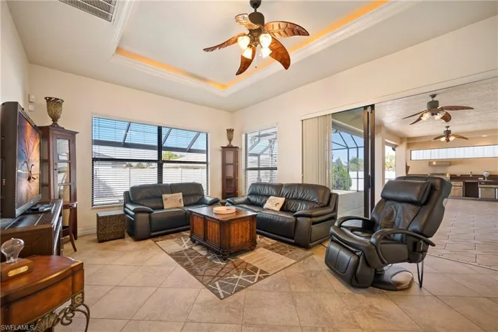 Living room with ceiling fan, healthy amount of natural light, a raised ceiling, light tile patterned floors, and crown molding