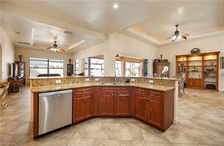 Kitchen featuring a tray ceiling, ceiling fan, open floor plan, dishwasher, and light stone counters