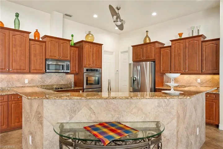 Kitchen featuring decorative backsplash, wood finish cabinetry, light stone counters, stainless steel appliances, and light tile patterned flooring
