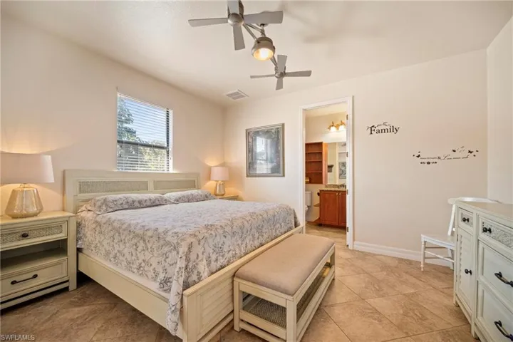 Bedroom featuring ceiling fan, light tile patterned flooring, and ensuite bath