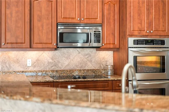 Kitchen featuring stainless steel appliances, light stone countertops, wood finish cabinetry, and tasteful backsplash