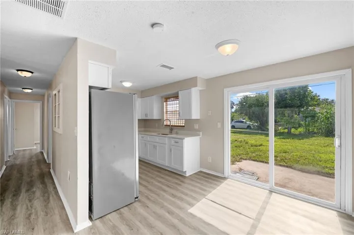 Kitchen with freestanding refrigerator, light wood finished floors, white cabinetry, light countertops, and a textured ceiling