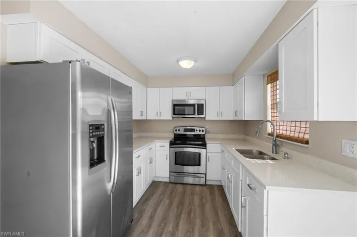 Kitchen with stainless steel appliances, white cabinetry, and dark wood finished floors