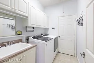 Washroom featuring cabinets, sink, washing machine and clothes dryer, and light tile patterned floors