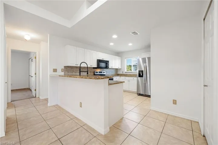 Kitchen featuring a peninsula, backsplash, white cabinets, stainless steel appliances, and dark stone countertops