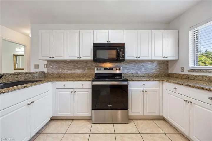 Kitchen with stainless steel electric range, white cabinetry, black microwave, and dark stone countertops