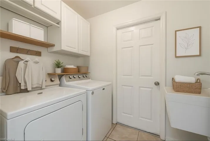 Washroom with light tile patterned flooring, washing machine and clothes dryer, and cabinet space